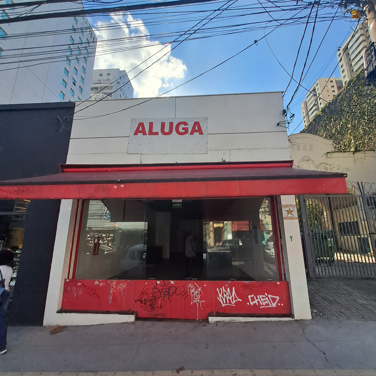 Antes: o imóvel sem a estrutura da loja, com fachada vermelha e placa ALUGA sem telefone